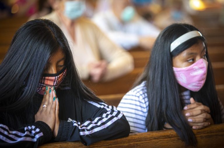 Two girls wearing face masks pray during a Sept. 26, 2020, Mass at St