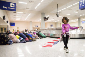 A young girl dances with an American flag at Dallas/Fort Worth International Airport in Dallas Jan. 29 as women pray during a protest against a travel ban imposed by U.S. President Donald Trump's executive action. (CNS photo/Laura Beckman, Reuters) See TRUMP-REFUGEES-REACTION Jan. 30, 2017.