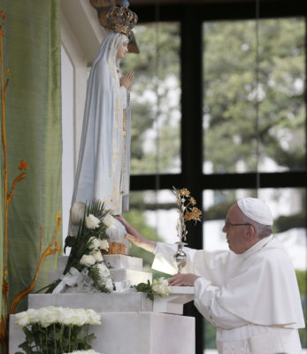 Pope Francis places flowers near a statue of Mary as he prays in the Little Chapel of the Apparitions at the Shrine of Our Lady of Fatima in Portugal, May 12. The pope was making a two-day visit to Fatima to commemorate the 100th anniversary of the Marian apparitions and to canonize two of the young seers. (CNS photo/Paul Haring) See POPE-FATIMA-VIGIL May 12, 2017.