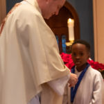 Msgr. Christopher Connelly, rector of St. Michael's Cathedral, presents a ribbon to a member of the Cathedral Choir of Boys and Adults on Novice Chorister Ribbon Day.