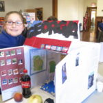 Fourth-grader Georgia Payette welcomes visitors to Georgia during State Box Exhibit Day at St. Joan of Arc School.