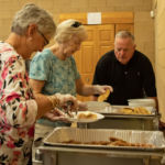 Sister of St. Joseph Eileen Sullivan, pastoral minister; a parish volunteer; and Deacon Leo Coughlin, director of the diocesan diaconate formation program, serve at the End-of-Summer Pancakes event at St. Michael's Cathedral.